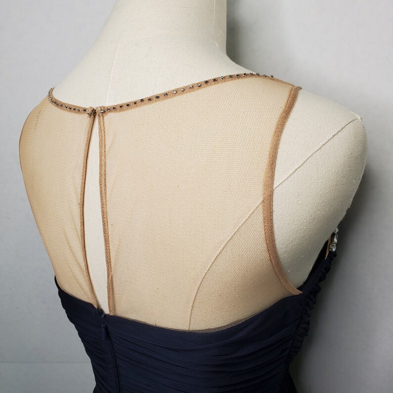 May include: A navy blue sleeveless dress with a sheer mesh panel at the back. The mesh panel is adorned with small rhinestones around the neckline.