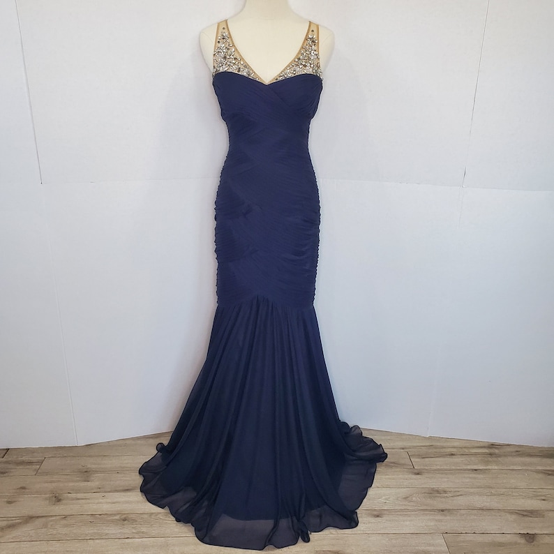 May include: A navy blue, floor-length, sleeveless gown with a sweetheart neckline and a beaded embellishment at the neckline.