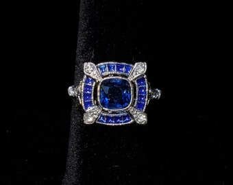 May include: A silver ring with a large blue gemstone surrounded by smaller blue gemstones and white diamonds.