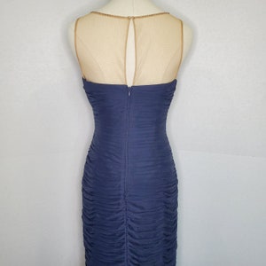May include: A navy blue sleeveless dress with a sheer mesh back panel and a zipper closure. The dress has a ruched design and a fitted silhouette.