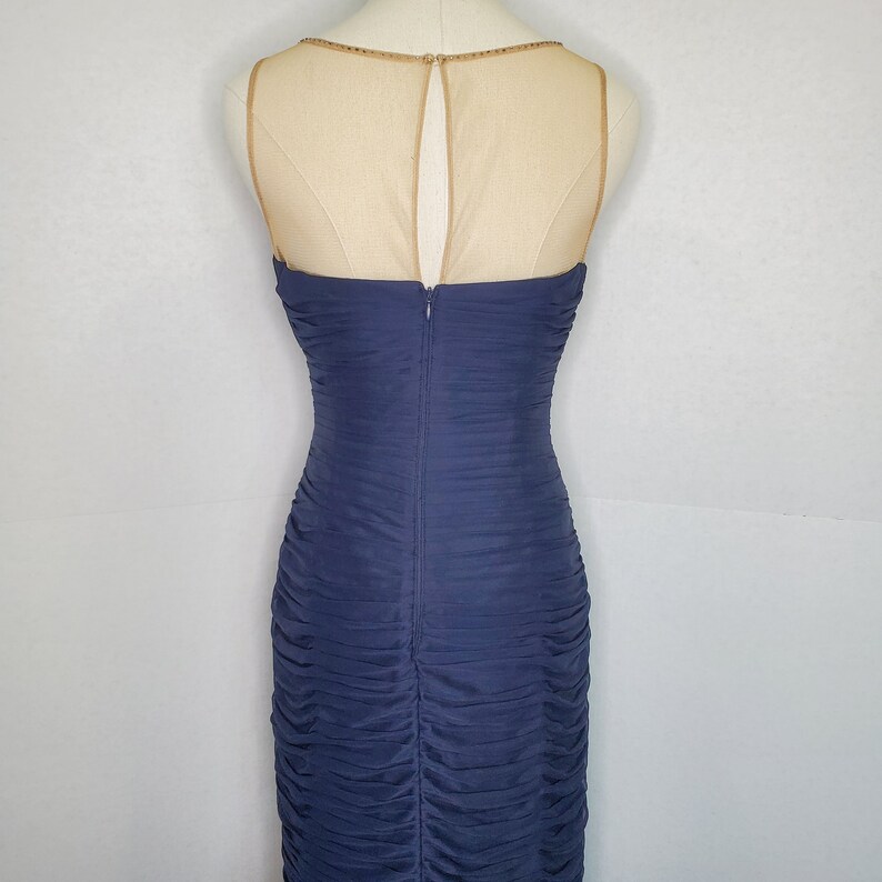 May include: A navy blue sleeveless dress with a sheer mesh back panel and a zipper closure. The dress has a ruched design and a fitted silhouette.