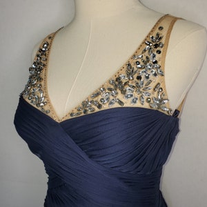 May include: A navy blue sleeveless dress with a V-neckline and a beaded embellishment on the neckline.