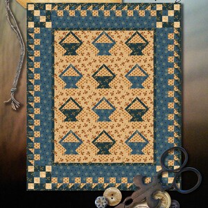 Może przedstawiać: Wzór patchworku o nazwie "Blissfully Blue" autorstwa Marty Walker, z motywem koszyka w odcieniach niebieskiego i brązowego. Wzór ma 26 cali na 32 cali i jest dostępny w Wagons West Designs.