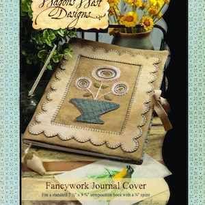May include: A beige journal cover with a floral embroidery. The cover has a scalloped edge and a central embroidered flower design. It fits a 19 cm x 24.8 cm composition book. The text "Fancywork Journal Cover" is displayed. The cover is from Hagons Nest Designs.