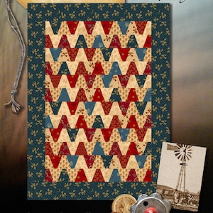 May include: Tumbleweed quilt pattern by Martha Walker, featuring a chevron design in red, blue and cream fabrics. The pattern is from Wagon's West Designs and measures 21 1/2 inches by 16 inches.