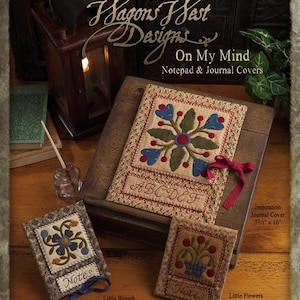 May include: A collection of three quilted fabric journal and notepad covers. The covers feature floral designs in shades of blue, red, and green. The covers are labeled "Notes" and have a ribbon tie. The largest cover is 7 1/2 inches by 10 inches and is labeled "Inspiration Journal Cover". The smaller covers are 4 1/2 inches by 5 1/2 inches and are labeled "Little Wreath Notepad Cover" and "Little Flowers Notepad Cover".