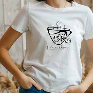 Puede incluir: Camiseta blanca con una ilustración negra de una taza de té humeante y el texto "Cha khoo".