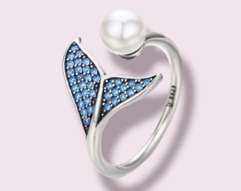 May include: A silver ring with a blue crystal whale tail design and a pearl accent. The ring is adjustable and has a '925' stamp on the band.
