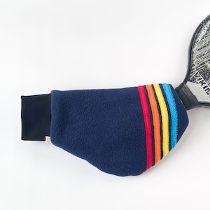 May include: A navy blue tennis racket cover with a black cuff and a rainbow stripe design. The cover is made of a soft, textured material and is designed to protect the racket head.