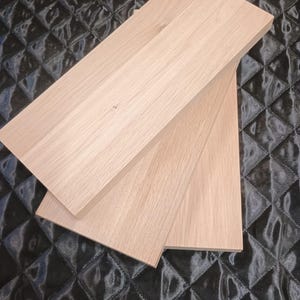 Può includere: Tre assi di legno di colore chiaro, forse per scaffalature o un progetto simile, sono impilate ad angolo. La venatura del legno è visibile. Le assi sono appoggiate su uno sfondo nero trapuntato.