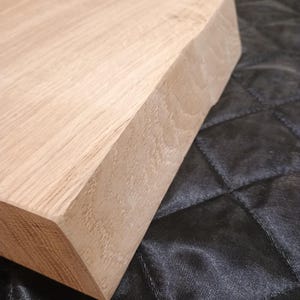 Può includere: Primo piano di un blocco di legno non rifinito di colore chiaro con un bordo smussato. La venatura del legno è visibile e il blocco poggia su una superficie scura e strutturata. L'angolo del blocco è angolato.