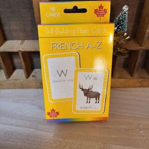 Peut inclure: Une bo&icirc;te jaune de cartes flash pour l'apprentissage du fran&ccedil;ais A-Z. La bo&icirc;te porte l'inscription "48 cartes" et "Fran&ccedil;ais A-Z". Les cartes flash pr&eacute;sentent la lettre "W" avec le mot fran&ccedil;ais "wapiti" et une illustration d'un wapiti.