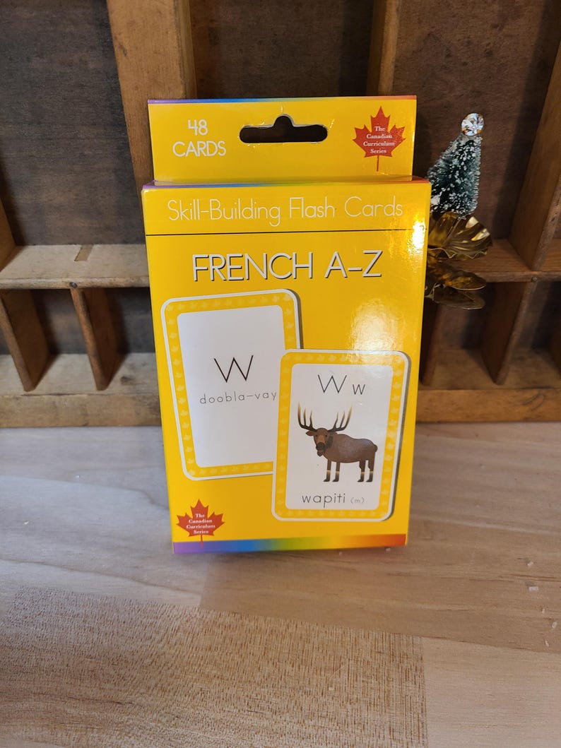 Peut inclure: Une bo&icirc;te jaune de cartes flash pour l'apprentissage du fran&ccedil;ais A-Z. La bo&icirc;te porte l'inscription "48 cartes" et "Fran&ccedil;ais A-Z". Les cartes flash pr&eacute;sentent la lettre "W" avec le mot fran&ccedil;ais "wapiti" et une illustration d'un wapiti.
