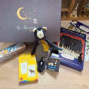 Peut inclure: Ensemble de jouets et de mat&eacute;riel &eacute;ducatif pour enfants. Comprend une peluche ours, des cartes de l'alphabet, des ombres chinoises et une bo&icirc;te avec un croissant de lune. Le texte "Les Moustaches" est visible sur la bo&icirc;te.