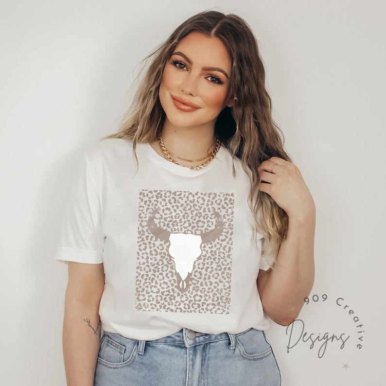 May include: White t-shirt with a brown and white leopard print design featuring a white bull skull. The design is centered on the shirt.