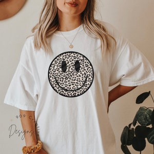 Peut inclure: T-shirt blanc avec un grand smiley imprim&eacute; l&eacute;opard noir et marron.