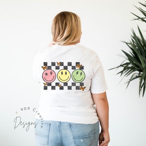 May include: White t-shirt with a checkered pattern, three smiley faces with different expressions, and orange butterflies. The smiley faces are pink, yellow, and green.