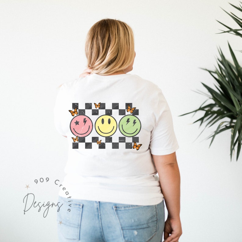 May include: White t-shirt with a checkered pattern, three smiley faces with different expressions, and orange butterflies. The smiley faces are pink, yellow, and green.