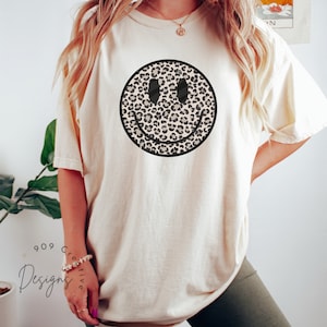 Peut inclure: Un t-shirt blanc avec un motif de smiley en imprim&eacute; l&eacute;opard noir et brun.