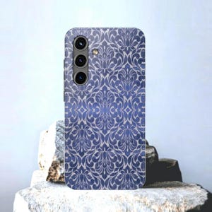 May include: A smartphone case with a blue and white floral damask pattern. The case has a camera array on the back and is displayed on a stone surface. The design is a repeating pattern of stylized leaves and flowers.