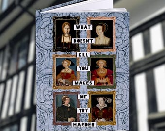 May include: A hardcover journal with a blue floral pattern and portraits of historical figures. The text "WHAT DOESN'T KILL YOU MAKES ME TRY HARDER" is displayed. The journal is open, revealing blank pages.