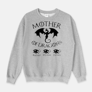 Pu&ograve; includere: Felpa grigia con il testo "Mother of Dragons" e una grafica di drago nero. Sotto il testo ci sono tre grafiche di draghi pi&ugrave; piccole con i nomi "Rachael", "Dylan" e "Zachary" sotto.