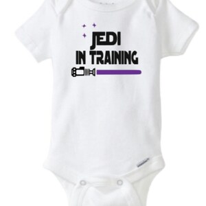May include: White baby onesie with black text that reads "Jedi in Training" and a purple lightsaber graphic.
