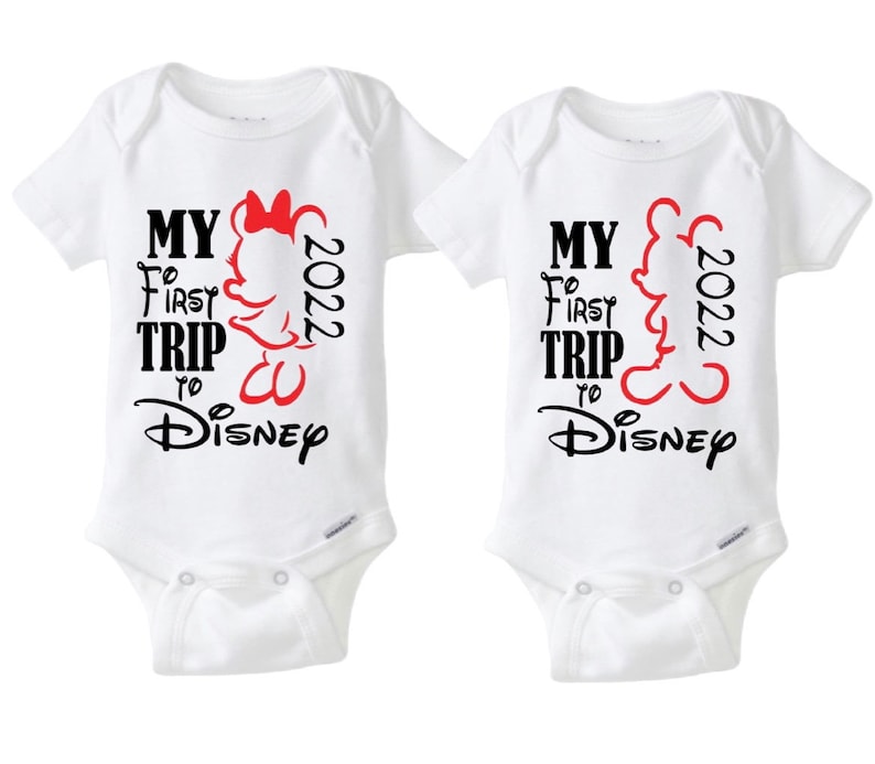 May include: Two white baby onesies with the text "MY FIRST TRIP to Disney 2022". One onesie features a red Minnie Mouse silhouette, and the other features a red Mickey Mouse silhouette. The text is in black and red.