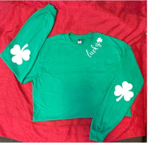 May include: Green long-sleeved shirt with white shamrock designs on the sleeves and the word "lucky" on the shoulder.