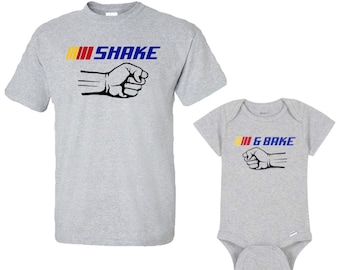 May include: Gray t-shirt with a black fist and the text "SHAKE" in blue and yellow. A gray baby onesie with a black fist and the text "& BAKE" in blue and yellow.