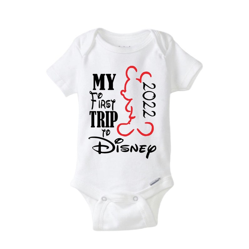 May include: White baby onesie with short sleeves. The onesie has the text "MY FIRST TRIP TO Disney 2022" in black and red. A red outline of Mickey Mouse is on the right side of the text.