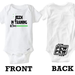 May include: White baby onesie with the text "Jedi in Training" and a green lightsaber graphic on the front. The back of the onesie has the text "Pew Pew Pew" in a black box.
