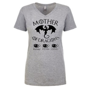 Pu&ograve; includere: Maglietta grigia a collo a V con un motivo di drago nero e il testo "Mother of Dragons" con i nomi "Rachael", "Dylan" e "Zachary" sotto.