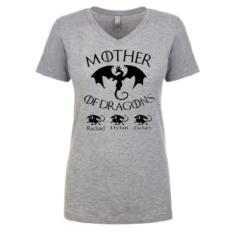 Pu&ograve; includere: Maglietta grigia a collo a V con un motivo di drago nero e il testo "Mother of Dragons" con i nomi "Rachael", "Dylan" e "Zachary" sotto.