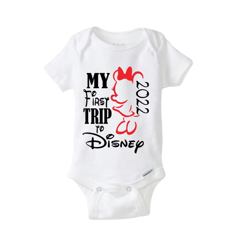 May include: White baby onesie with the text "MY FIRST TRIP to Disney 2022" in black and red. A Minnie Mouse graphic is on the right side. The onesie has short sleeves and a snap closure.