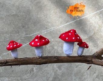 Peut inclure: Quatre décorations de champignons en feutre, avec des chapeaux rouges et des pois blancs, perchées sur une branche brune. Les champignons ont des tiges blanches. Le texte "PDF PATTERN" est inclus.