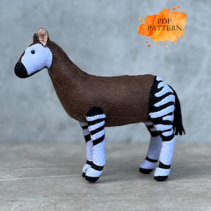 May include: A handmade plush okapi toy. The okapi has a brown body, a white and black striped pattern on its legs, and a light blue face. The text "PDF PATTERN" is in an orange watercolor splash in the upper right corner.