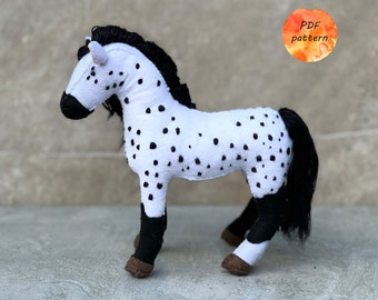 May include: A white and black spotted horse plush toy with a black mane and tail. The toy is standing on a gray surface. PDF pattern.