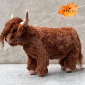 Könnte beinhalten: Ein braunes Stofftier einer Highland-Kuh mit langem, zotteligem Fell und kleinen, gebogenen Hörnern. Die Kuh steht, mit detailliertem Gesicht. Der Text "PDF PATTERN" ist in einem orangefarbenen Aquarell-Spritzer enthalten.