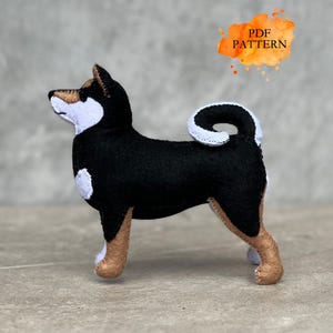 Puede incluir: Figura de perro Shiba Inu hecha a mano en fieltro. El perro es negro con marcas blancas y patas color canela. La imagen incluye el texto "PDF PATTERN" en estilo acuarela.