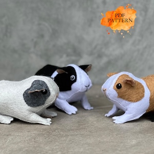 May include: Three handmade felt guinea pig toys in white, black, and brown. The guinea pigs have detailed features and are posed on a neutral surface. The image includes the text "PDF PATTERN" in an orange watercolor style.