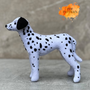 Peut inclure: Un chien dalmatien en feutre blanc avec des taches noires. Le chien est debout sur une surface grise. L'image comprend le texte "PDF PATTERN".