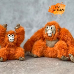 May include: Two plush orangutans, one with arms raised, the other seated. Both are orange with tan faces and hands. The text "PDF PATTERN" is in a watercolor-style bubble above the larger orangutan.