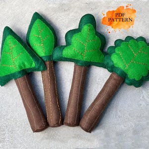 May include: Four handmade felt tree decorations with green leaves and brown trunks. The leaves have embroidered details, and the trunks are stitched. The image includes a watercolor splash with the text "PDF PATTERN".