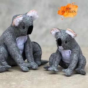 Op de afbeelding: Twee grijze vilten koala beer knuffels met witte borstvlekken, zwarte neuzen en kleine oren met roze accenten. De koala's zitten, en de afbeelding bevat een oranje en gele tekstbox in aquarel stijl met de tekst "PDF PATTERN".