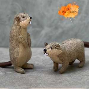 May include: Two felt beaver plush toys in shades of brown and beige. One beaver stands upright, the other is on all fours. The text "PDF PATTERN" is in an orange watercolor splash. These plushies are handmade.