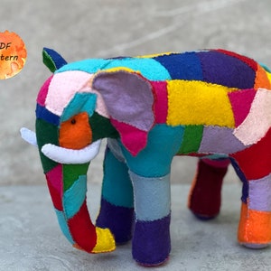 Può includere: Un giocattolo di elefante colorato a patchwork fatto di feltro. L'elefante è in piedi su una superficie grigia. Il giocattolo è fatto di molti colori diversi, tra cui rosso, blu, verde, giallo e viola.