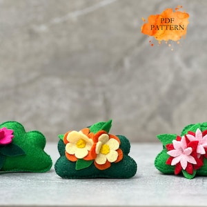 May include: Three handmade felt flower arrangements in green, with pink, yellow, and orange flower accents. The text "PDF PATTERN" is in an orange watercolor splash in the upper right corner. These are likely craft or DIY projects.