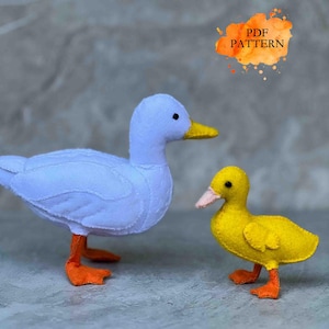 May include: Two felt duck toys. One is a light blue duck with orange feet and a yellow beak. The other is a smaller yellow duck with orange feet and a pink beak. The text "PDF PATTERN" is in an orange watercolor-style shape.