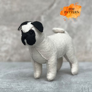 Könnte beinhalten: Ein weißer Filz-Mops mit schwarzen Ohren und Gesicht. Der Hund steht auf einer grauen Oberfläche. Der Text "PDF PATTERN" ist in der oberen rechten Ecke des Bildes sichtbar.